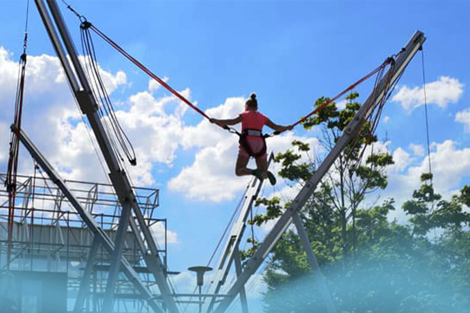 Besucherin schwebt am Bungee-Trampolin im Außenbereich des SkyandSand Trampolinparks Würzburg und erlebt pures Freiheitsgefühl.