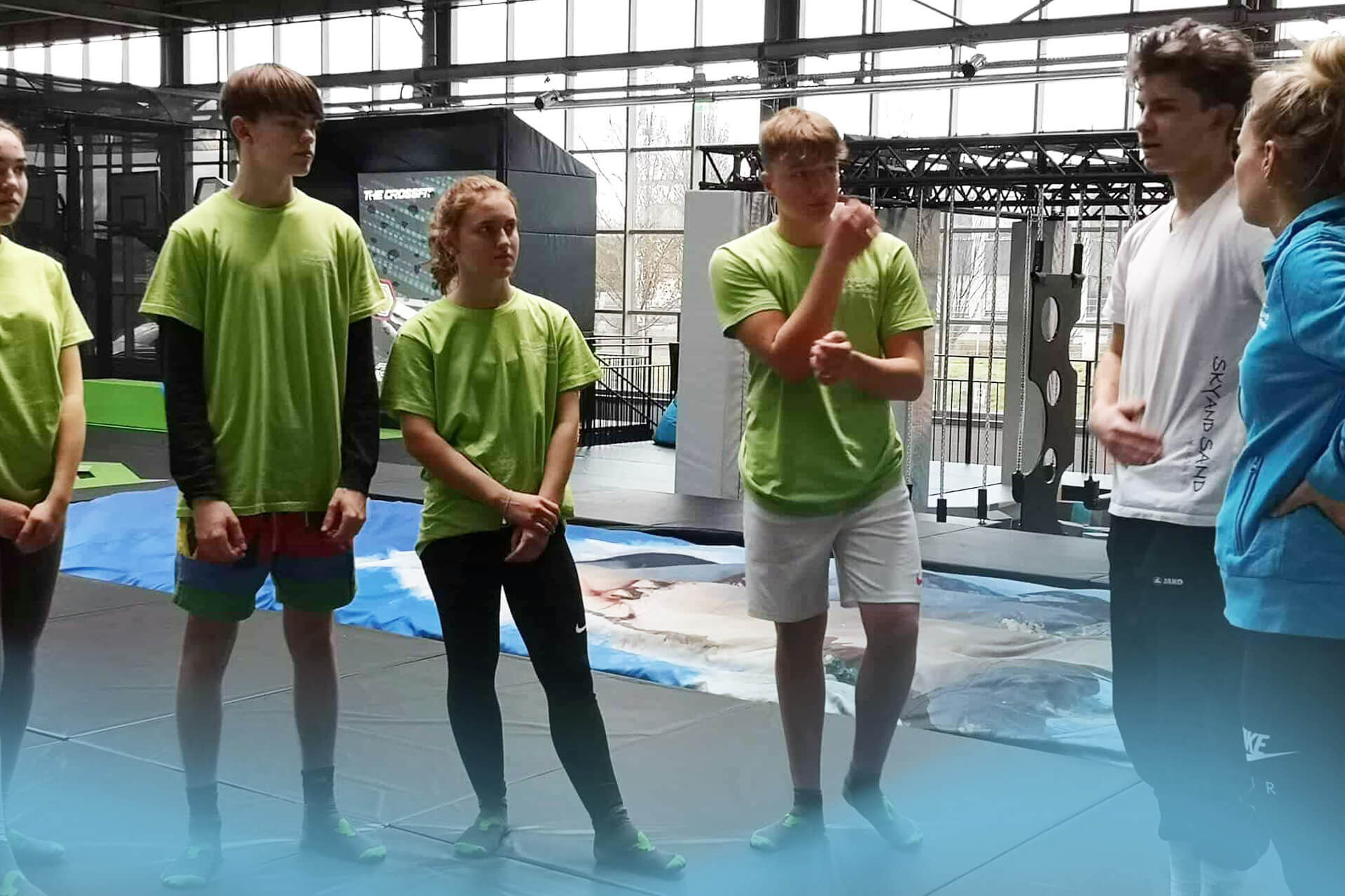 Jugendliche hören aufmerksam den Erklärungen eines Trainers bei einem betreuten Kurs im SkyandSand Trampolinpark Würzburg zu.
